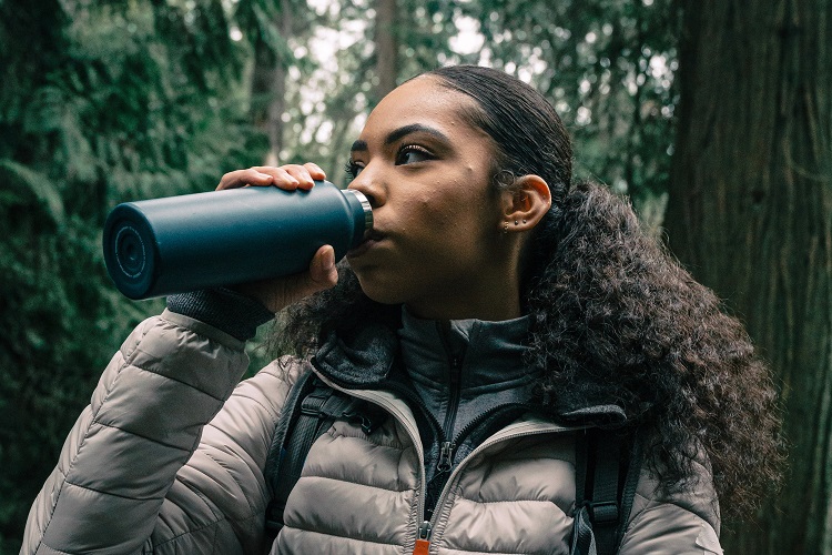 A woman drinking from a water bottle in the woods.